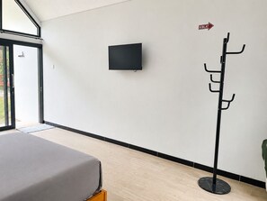 Ein modernes Zimmer mit einem Bett, einem Kleiderhaken, einem Fernseher und einer Tür, die nach draußen führt.