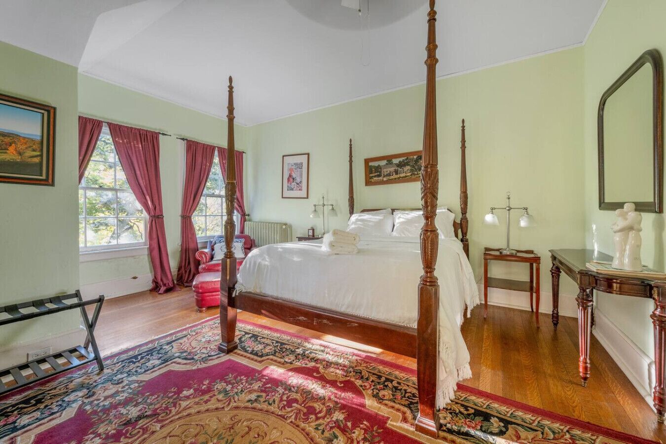 A four-poster bed in a room with a large window, a red chair, and a wooden floor.