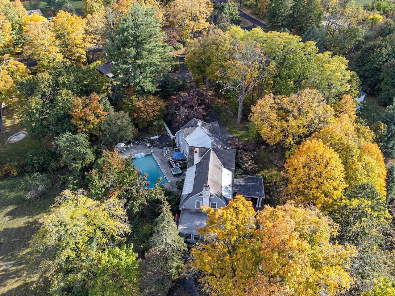 An aerial view of a house surrounded by autumn foliage, with a visible swimming pool and a large garage.