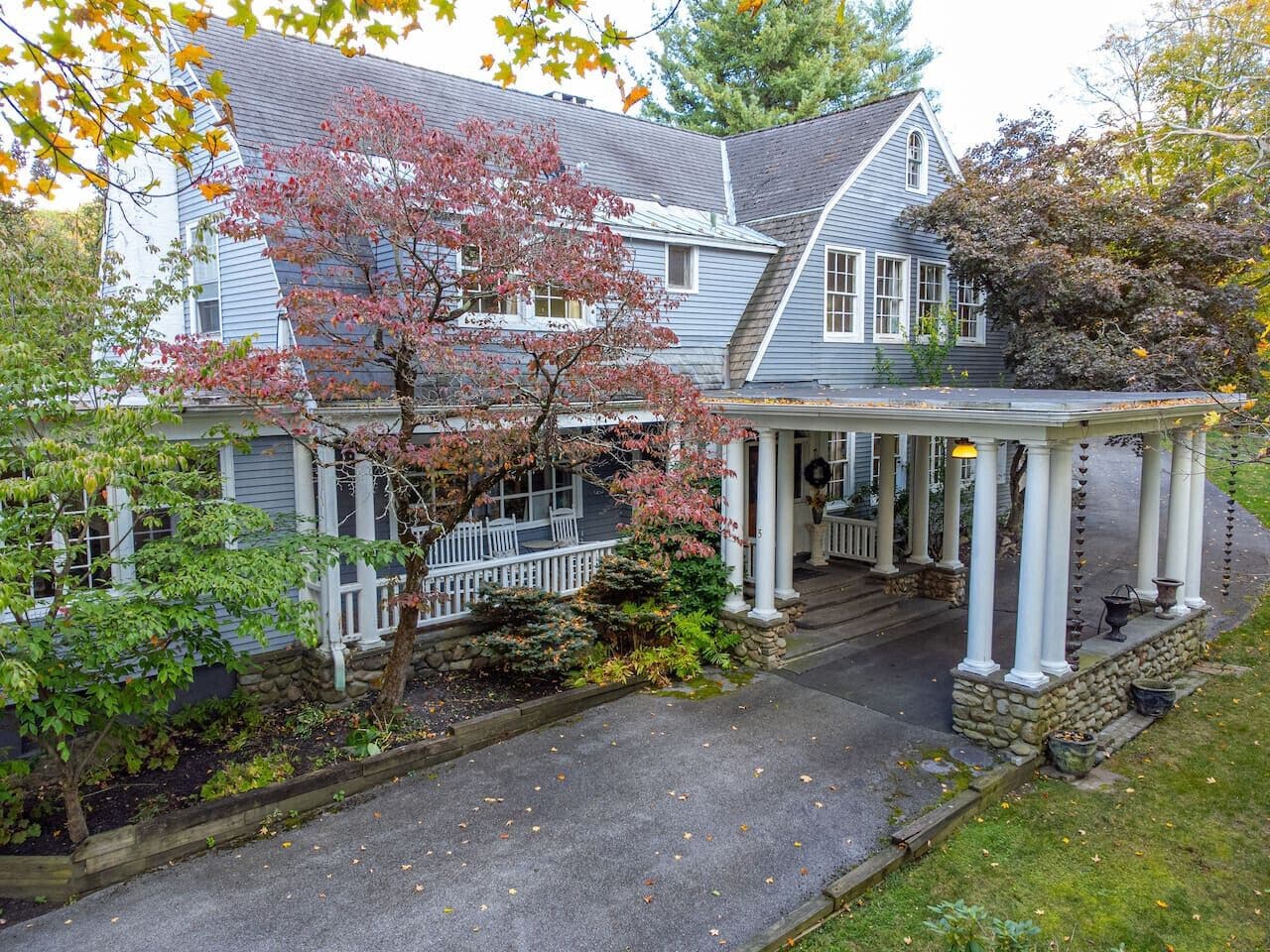 A two-story house with a porch, a stone foundation, and a driveway leading to the entrance.