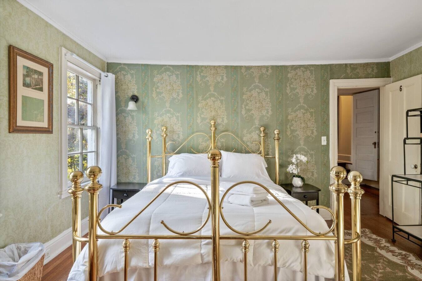 A room with a bed, a window, a door, and a wall with a patterned wallpaper.