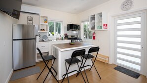 Una cucina moderna con frigorifero in acciaio inox, forno a microonde e piano cottura. Ci sono due sedie nere all'isola, e un lavello con una finestra sopra.