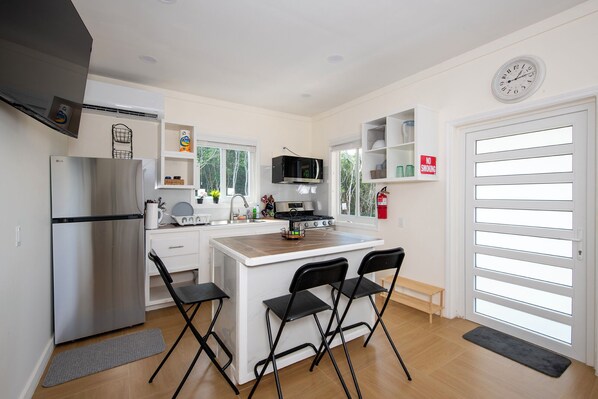 Una cocina moderna con un refrigerador de acero inoxidable, un microondas y una estufa. Hay dos sillas negras en la isla, y un fregadero con una ventana encima.