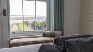 Una camera da letto con un letto, una finestra vista giardino e edifici, e una seduta finestrino con cuscino.