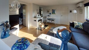 Ein modernes Wohnzimmer mit einer Couch, einem Couchtisch und dekorativen Glasvasen. Es gibt einen Fernseher, einen Kamin und eine Tür zu einem anderen Raum.