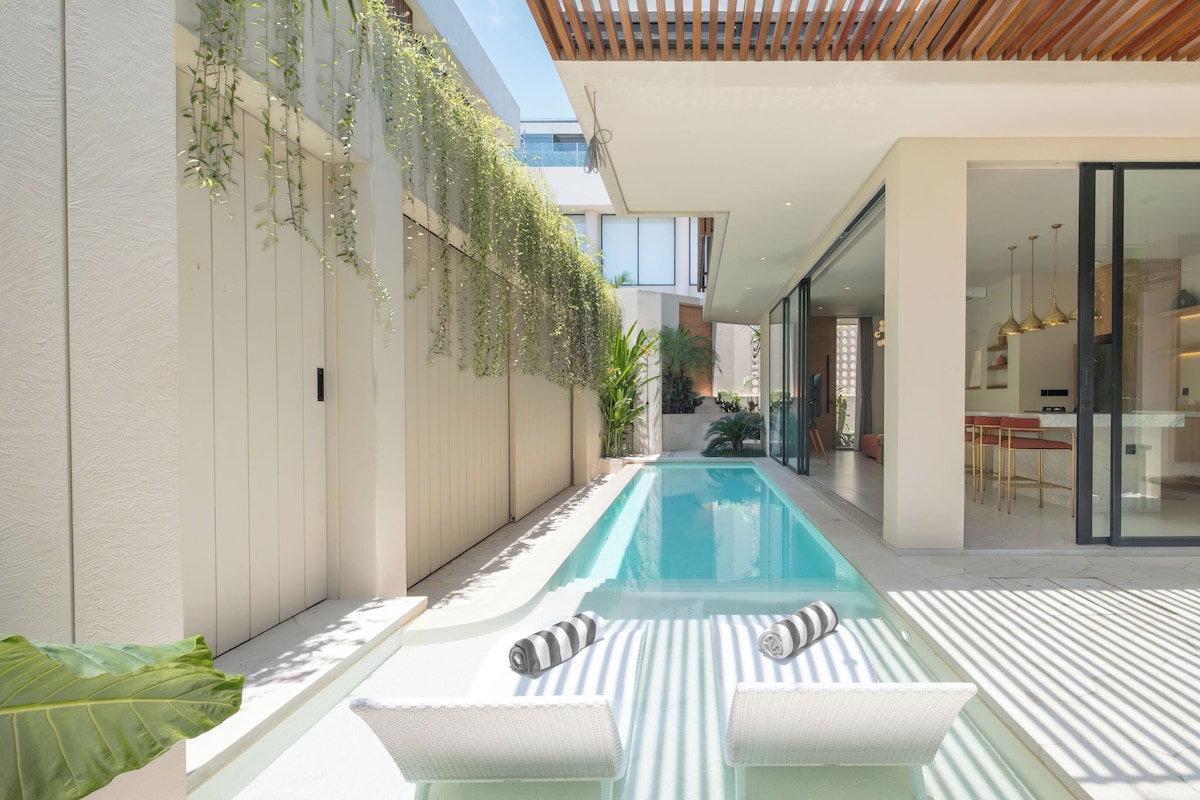 A modern outdoor pool area with a long, narrow pool, lounge chairs, and a pergola overhead.