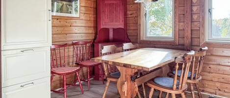 Interno di una baita in legno con un tavolo da pranzo, sedie rosse, un armadietto rosso e una finestra che si affaccia su alberi.