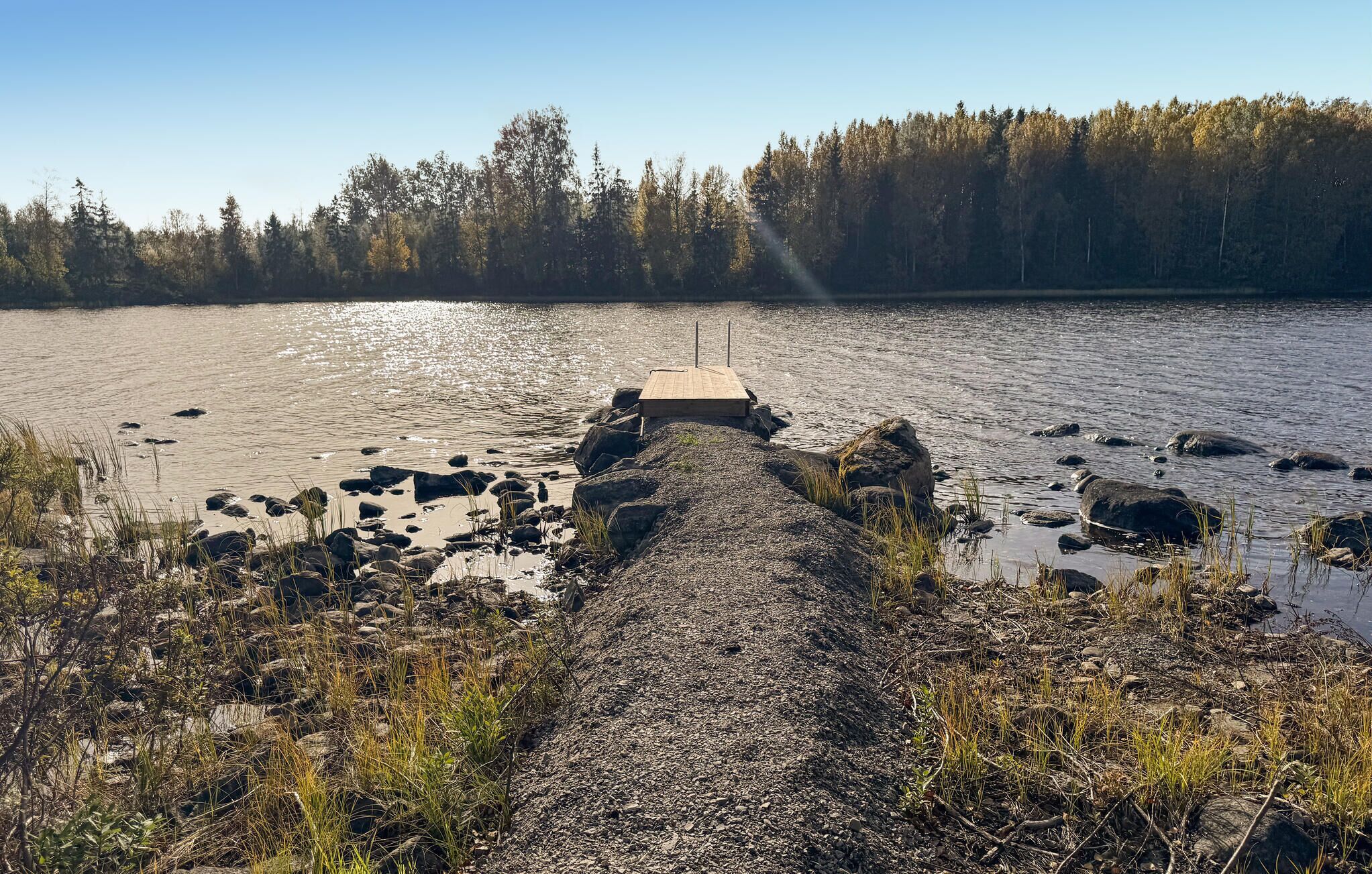 Une jetée en bois s’étendant sur un lac paisible, bordé de rochers et d’une végétation clairsemée.