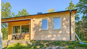 A wooden cabin with two windows, a covered porch with chairs, and a stone pathway leading to the entrance. - Gorgeous home in Rörvik with WiFi (Rörvik)