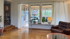 Una sala de estar con un sofá de cuero marrón, una mesa de centro de vidrio y vistas a un jardín a través de ventanas amplias.
