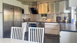 Una cocina moderna con armarios blancos, electrodomésticos de acero inoxidable y un comedor con sillas blancas.