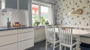 Una cocina con armarios blancos, una ventana con cortinas, una mesa de comedor con sillas y un reloj de pared.
