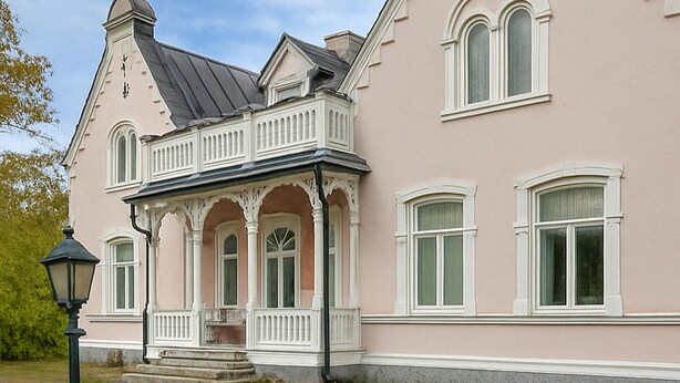 A pink building with a balcony, large windows, and a lamp post.