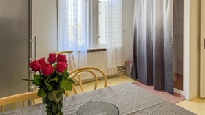 A dining area with a table set for two, a vase of red roses, and a window with white curtains.
