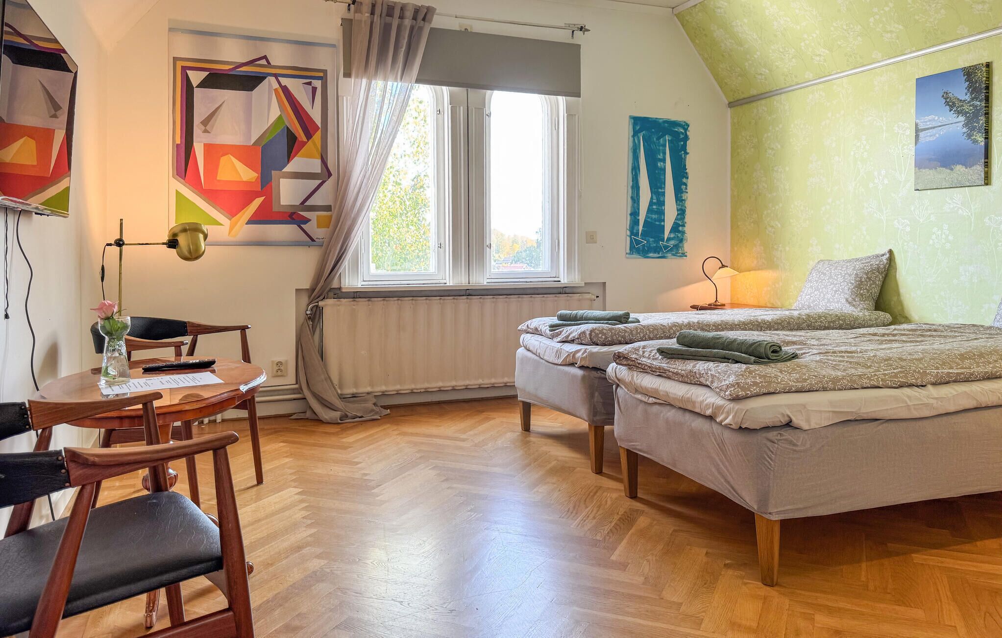 A room with a bed, a desk, and a chair. There is a window with curtains, a radiator, and a lamp.