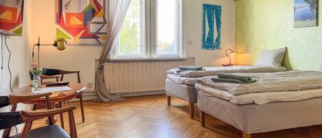A room with a bed, a desk, and a chair. There is a window with curtains, a radiator, and a lamp.