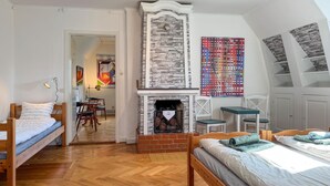A bedroom with a wooden bed, a fireplace, a dining area with chairs, and a colorful abstract painting.