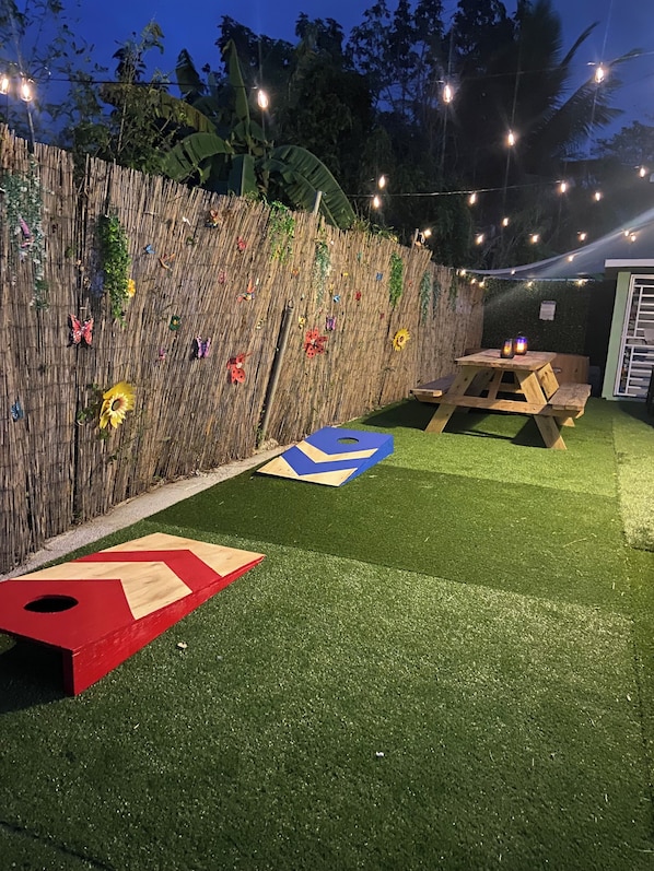 A backyard with artificial grass, a wooden picnic table, and a bamboo fence decorated with colorful items.