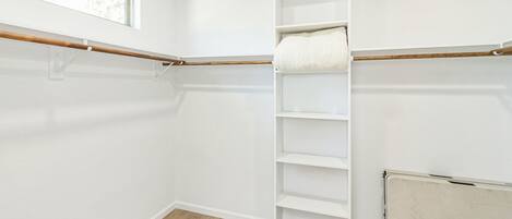 A walk-in closet with wooden flooring, white walls, and a window.