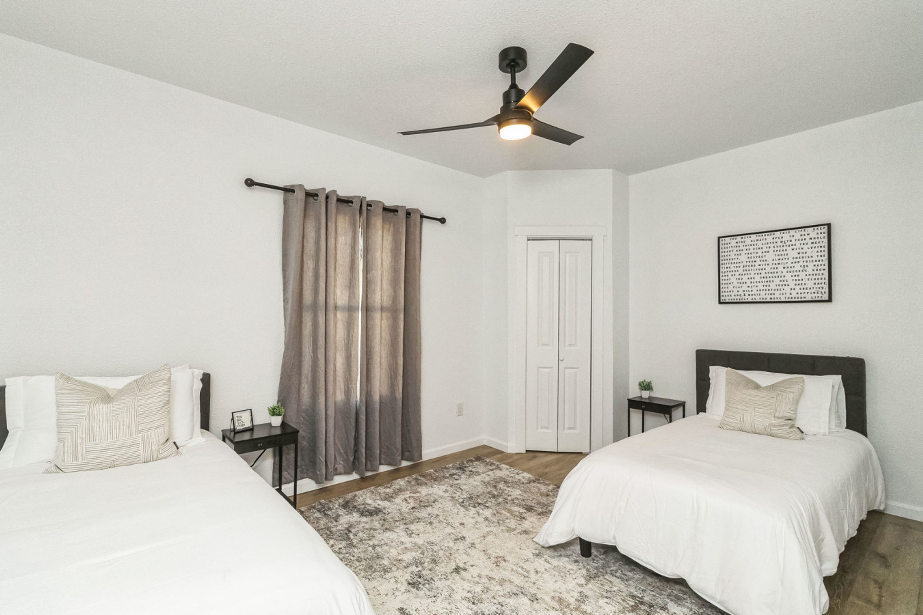 A bedroom with two beds, a ceiling fan, a door, and a rug.