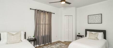 A bedroom with two beds, a ceiling fan, a door, and a rug.