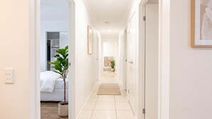 A hallway with a bed, a potted plant, and a door leading to a bathroom. - 4BDR Spacious Family Retreat (Logan Reserve)