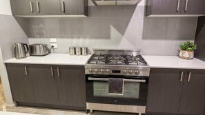 Une cuisine moderne équipée d’une cuisinière à gaz en acier inoxydable, d’un four et d’un plan de travail sur lequel se trouvent une bouilloire et une machine à café.