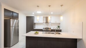 A modern kitchen with a stainless steel refrigerator, a gas stove, and pendant lighting.