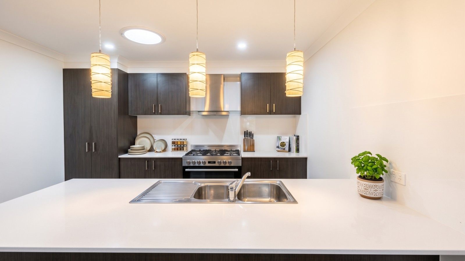 Una cocina moderna con una isla central, electrodomésticos de acero inoxidable, armarios oscuros e iluminación colgante.