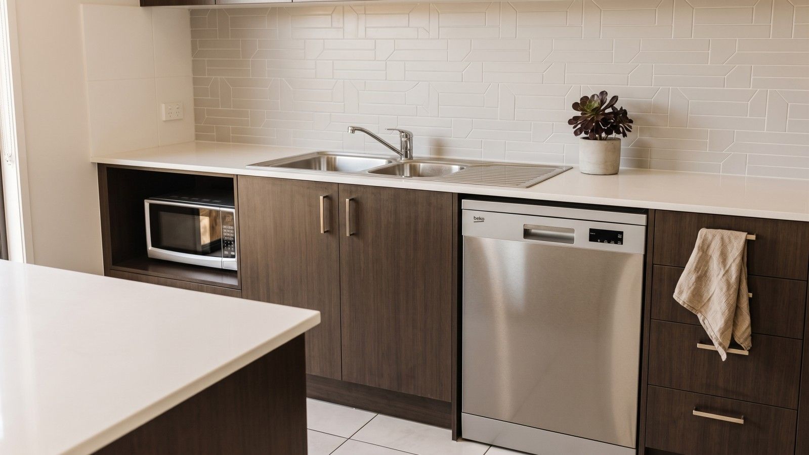 A modern kitchen with a built-in microwave, a stainless steel dishwasher, and a sink with a faucet.