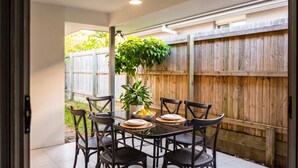 An outdoor patio with a round table, six chairs, a potted plant, and a wooden fence in the background. - 4BDR Spacious Family Retreat (Logan Reserve)