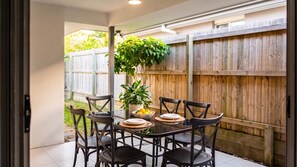 Eine Terrassesituation mit einem runden Tisch, sechs Stühlen, einem Blumentopf und einem Holzzaun im Hintergrund.