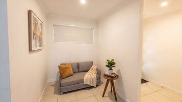 A corner room with a grey sofa, a small side table with a plant, and a framed picture on the wall.