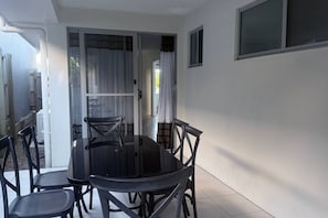 Zona pranzo con tavolo e sedie in vetro, una porta scorrevole che dà su un patio e vista sull'esterno.