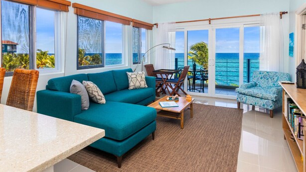 A spacious living room with a teal sofa, a dining table, and a view of the ocean through large windows. - Teal Horizon Oceanfrontcaribbean Escape Tower Isle (Tower Isle)