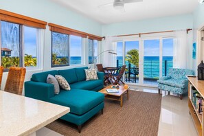 A spacious living room with a teal sofa, a dining table, and a view of the ocean through large windows. - Teal Horizon Oceanfrontcaribbean Escape Tower Isle (Tower Isle)