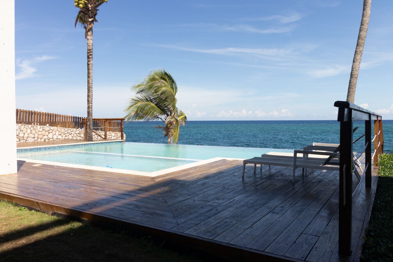 A wooden deck with a pool, palm trees, and a view of the ocean.