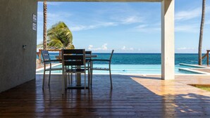 An outdoor seating area with a wooden deck, a table, and chairs facing a pool and the ocean. - Teal Horizon Oceanfrontcaribbean Escape Tower Isle (Tower Isle)