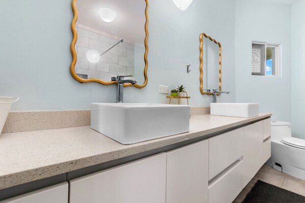 A modern bathroom with a white sink, a mirror with a gold frame, and a toilet. - Teal Horizon Oceanfrontcaribbean Escape Tower Isle (Tower Isle)