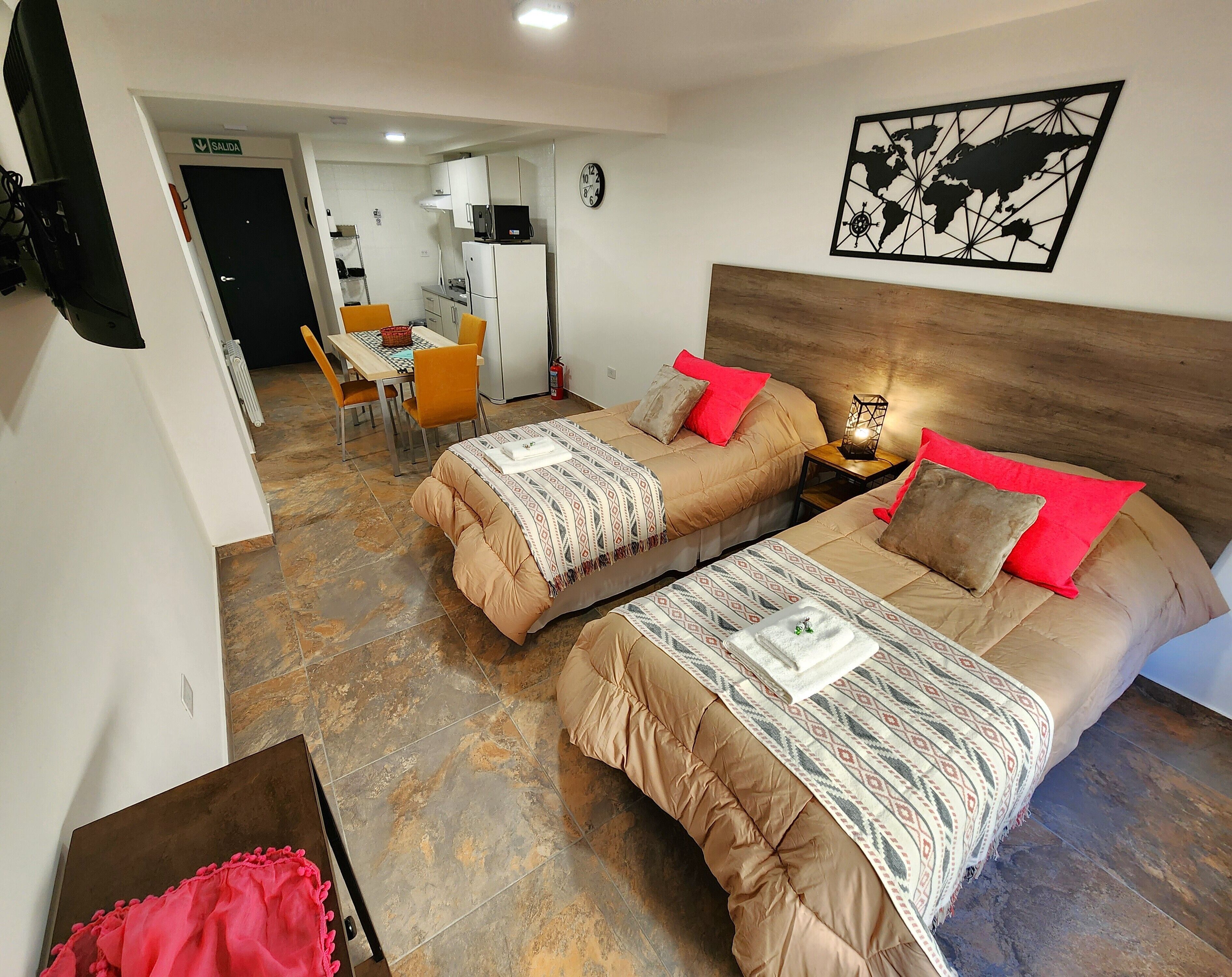 Habitación de hotel con dos camas, zona de comedor y cocina.
