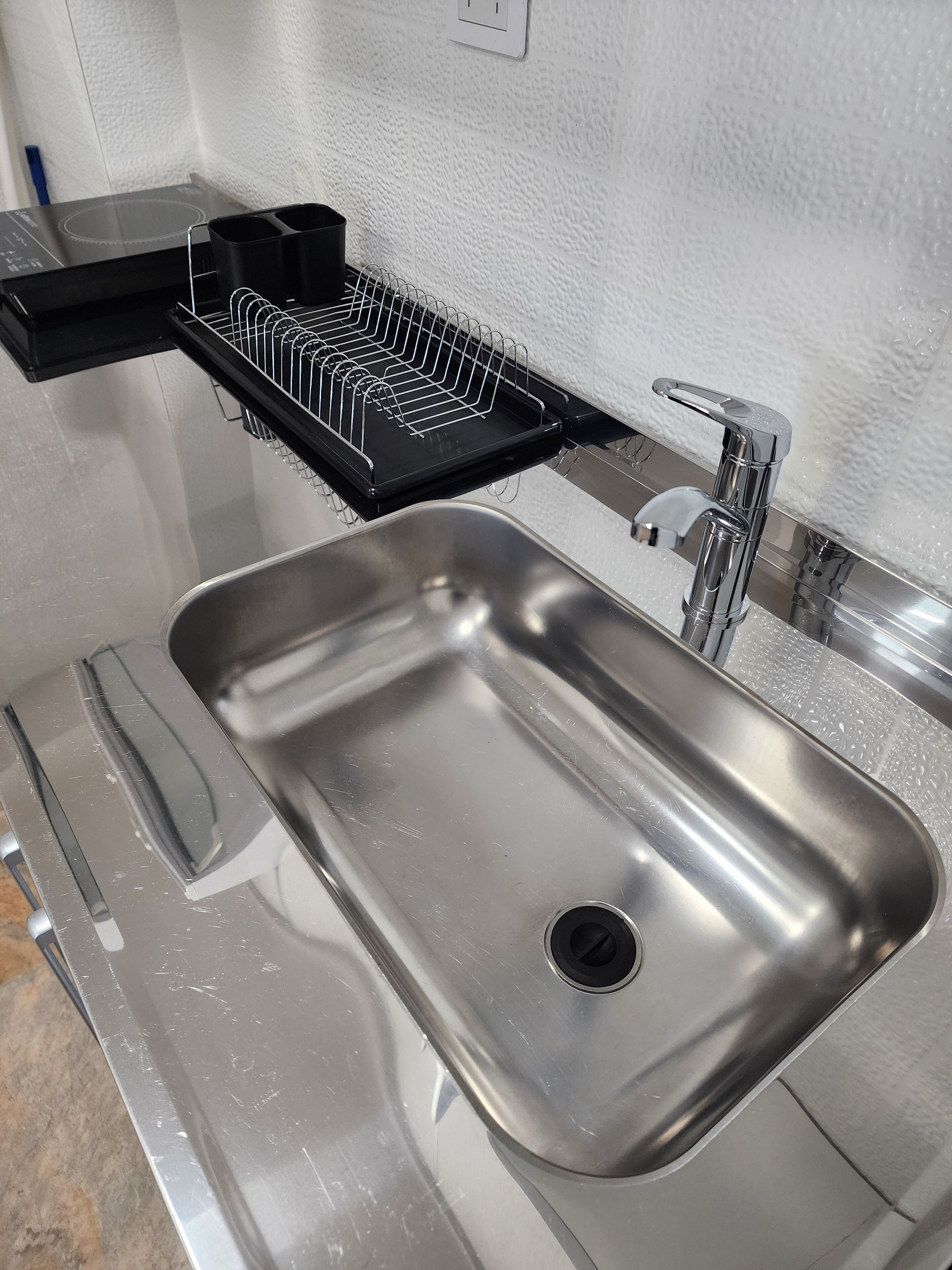 A stainless steel kitchen sink with a black drying rack and a modern faucet.