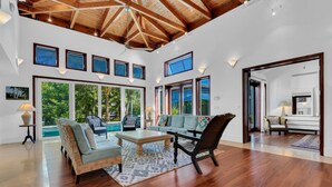 A spacious living area with a high ceiling, large windows, and a view of a pool.