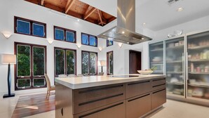 A modern kitchen with a large island, multiple windows, and a high ceiling with exposed beams.