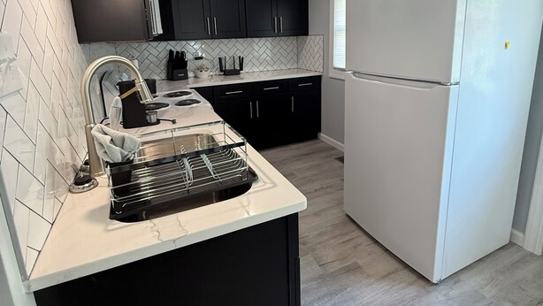 A modern kitchen with black cabinets, a white refrigerator, and a marble countertop.