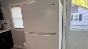 A compact kitchen with a white refrigerator, a window with blinds, and a door leading outside.