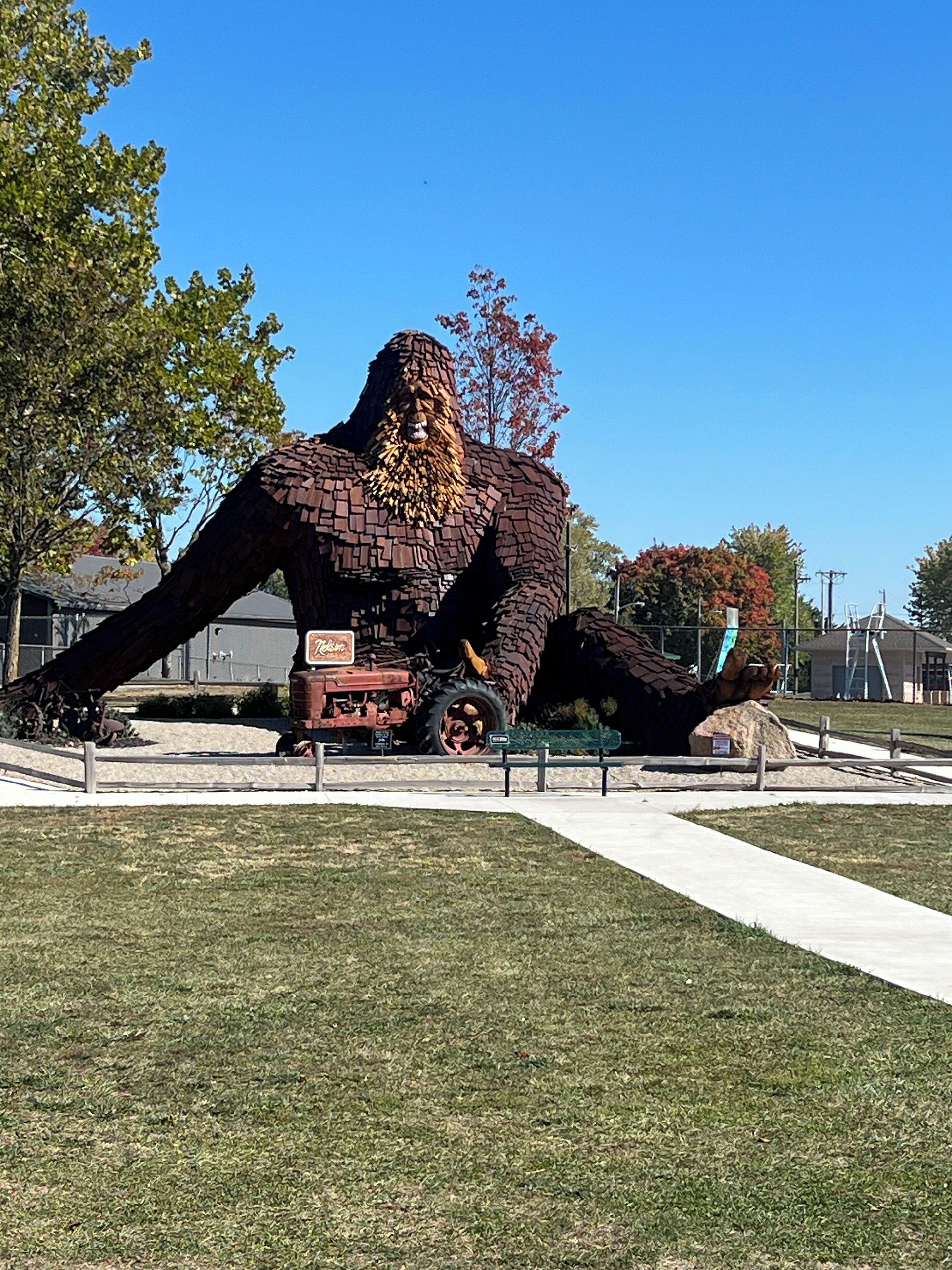 Una gran escultura de ladrillo que representa una figura con barba, ubicada en un área verde con un sendero pavimentado al frente.