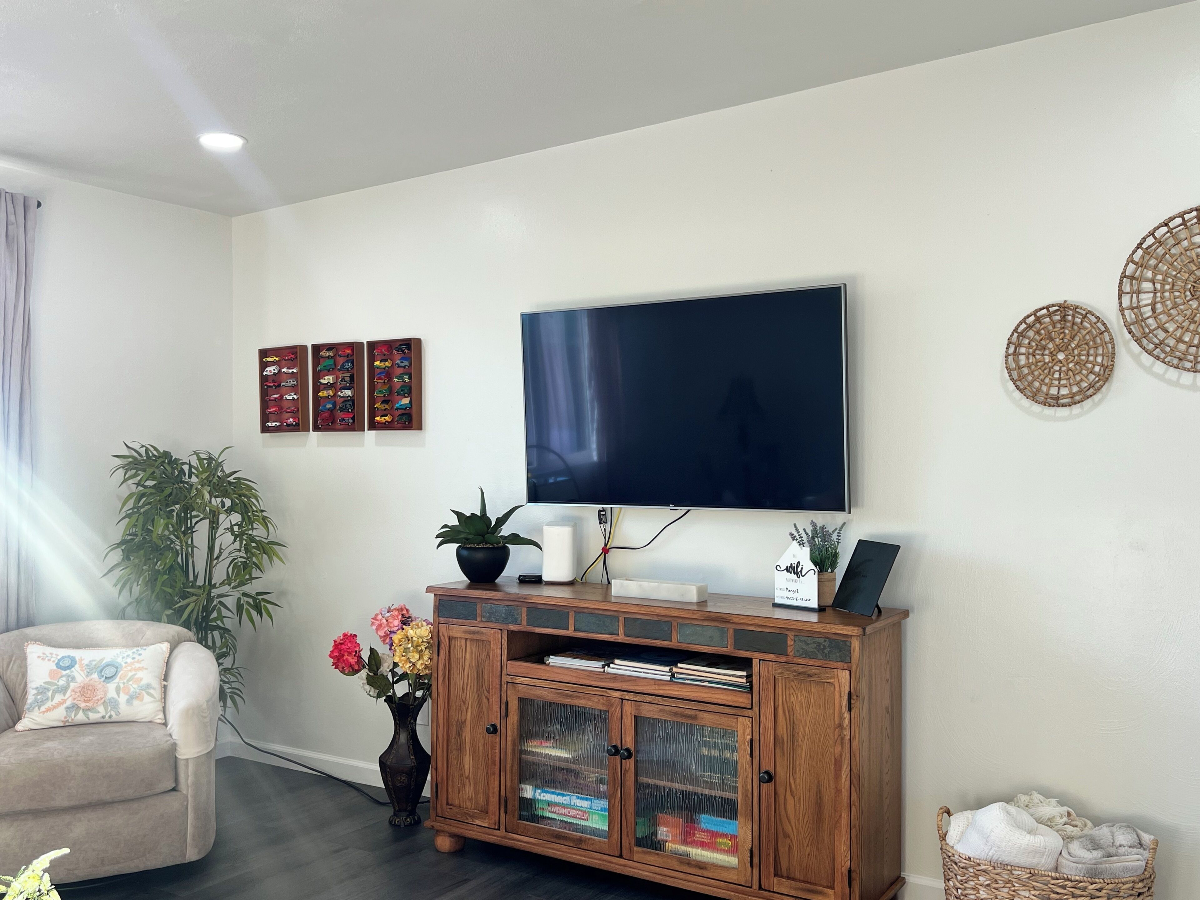 A living room with a flat-screen TV, wooden cabinet, and decorative items on the wall.