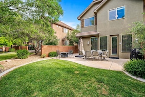 A residential house with a patio area, outdoor seating, and a well-maintained lawn.