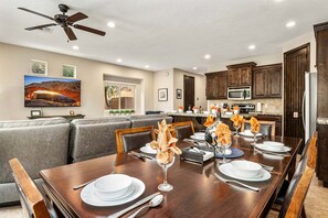 A dining area with a wooden table set for four, a ceiling fan, and a kitchen in the background.