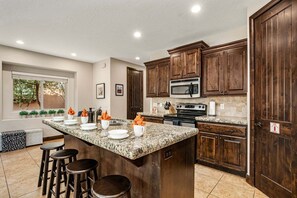 A kitchen with granite countertops, wooden cabinets, a large island with stools, a microwave, stove, and a sink.